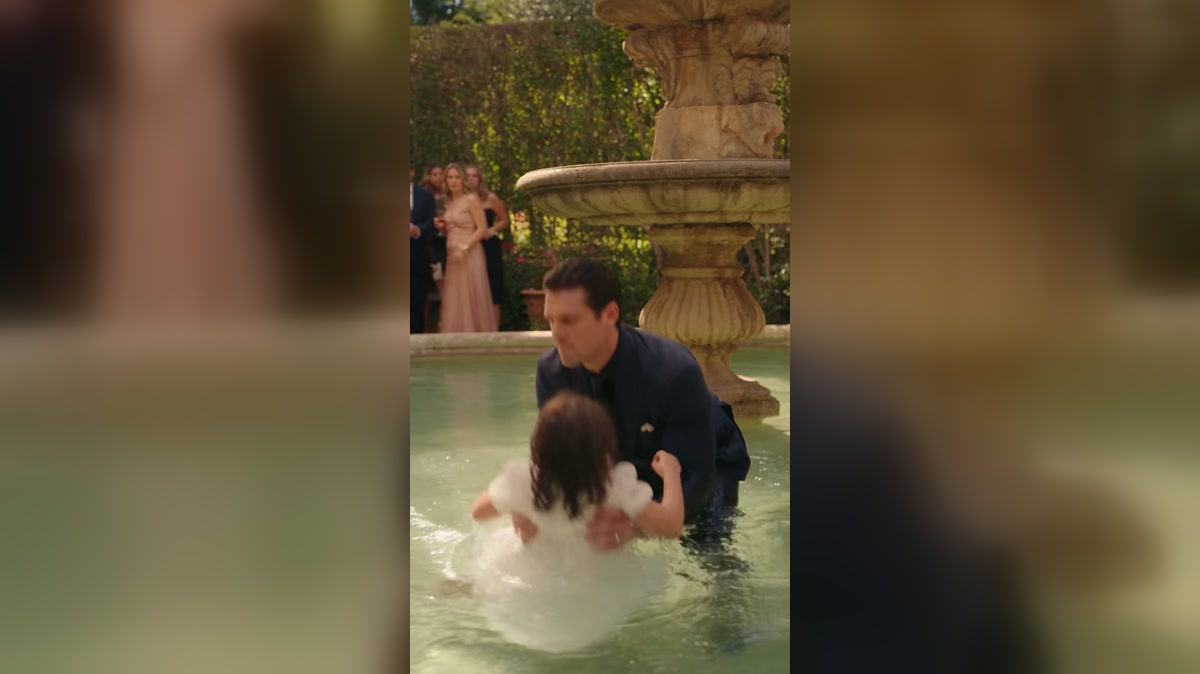 A man helps a woman from a courtyard fountain in a dramatized scene
