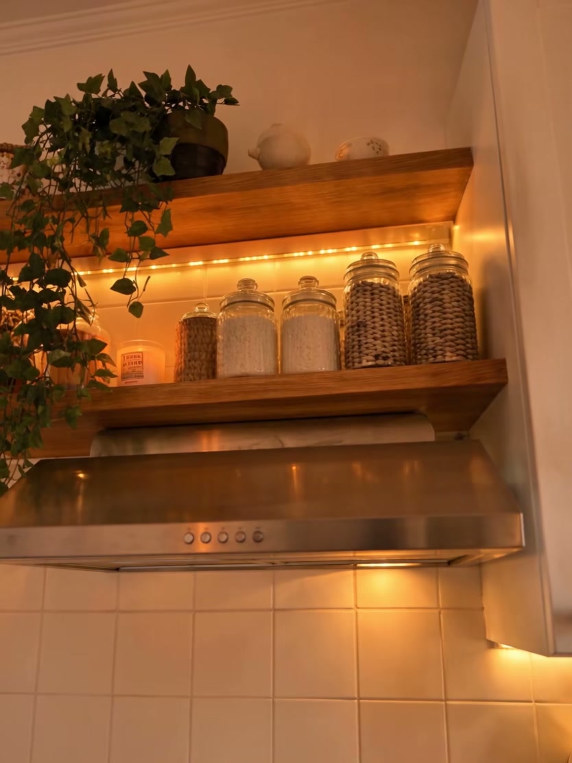 Open kitchen shelf styled with ceramics, plants, jars, and soft decorative lights
