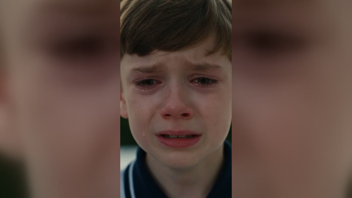 A tearful child looks up during a dramatized outdoor gathering