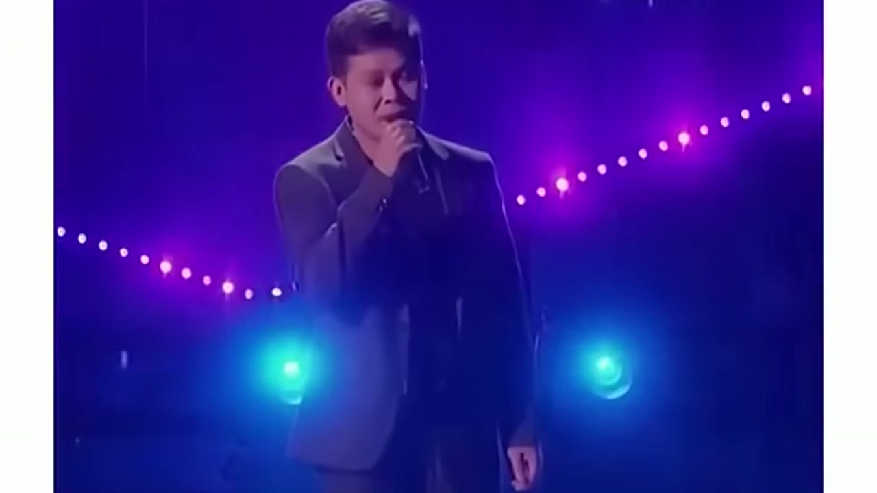 Marcelito Pomoy performing under blue and purple stage lights