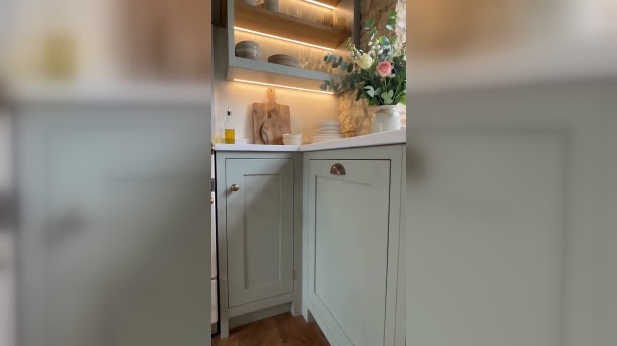 Warm open-shelf lighting highlights pottery and pale sage cabinet doors